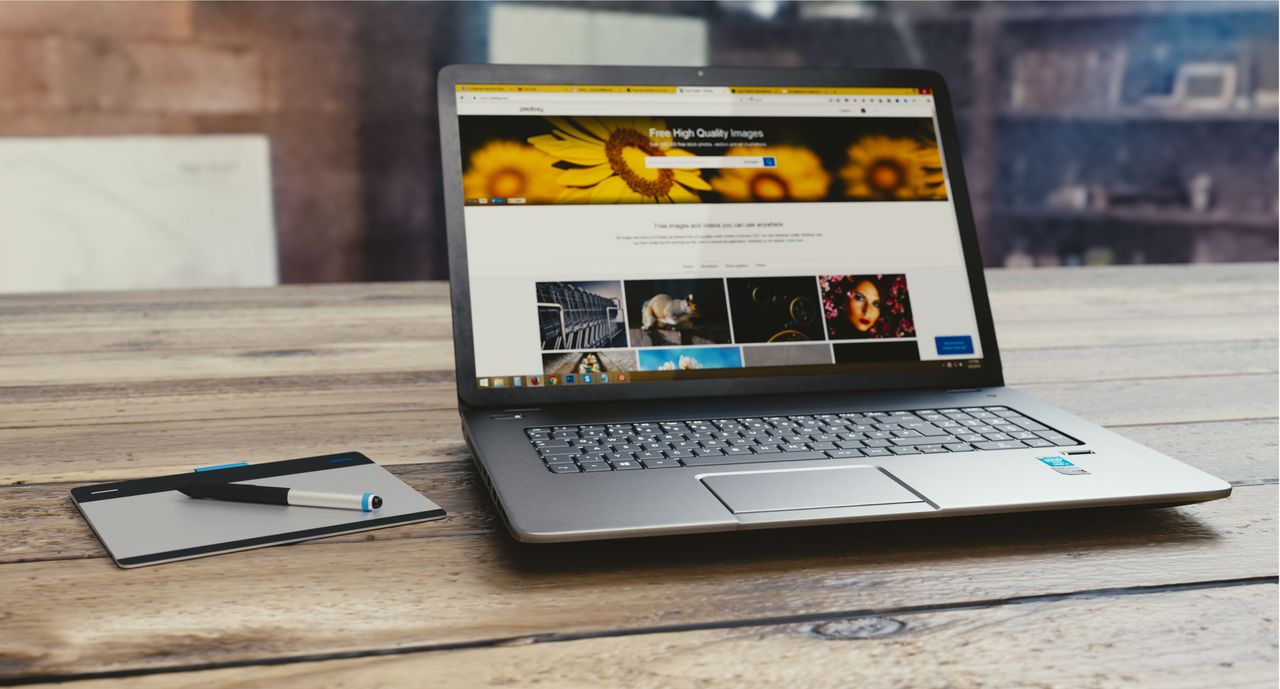 about-us-02 Laptop with open webpage on wooden desk, accompanied by tablet and pen, representing digital work setup.